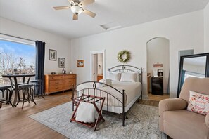 A bedroom with a bed, a desk, a chair, a dresser, and a window with a view.