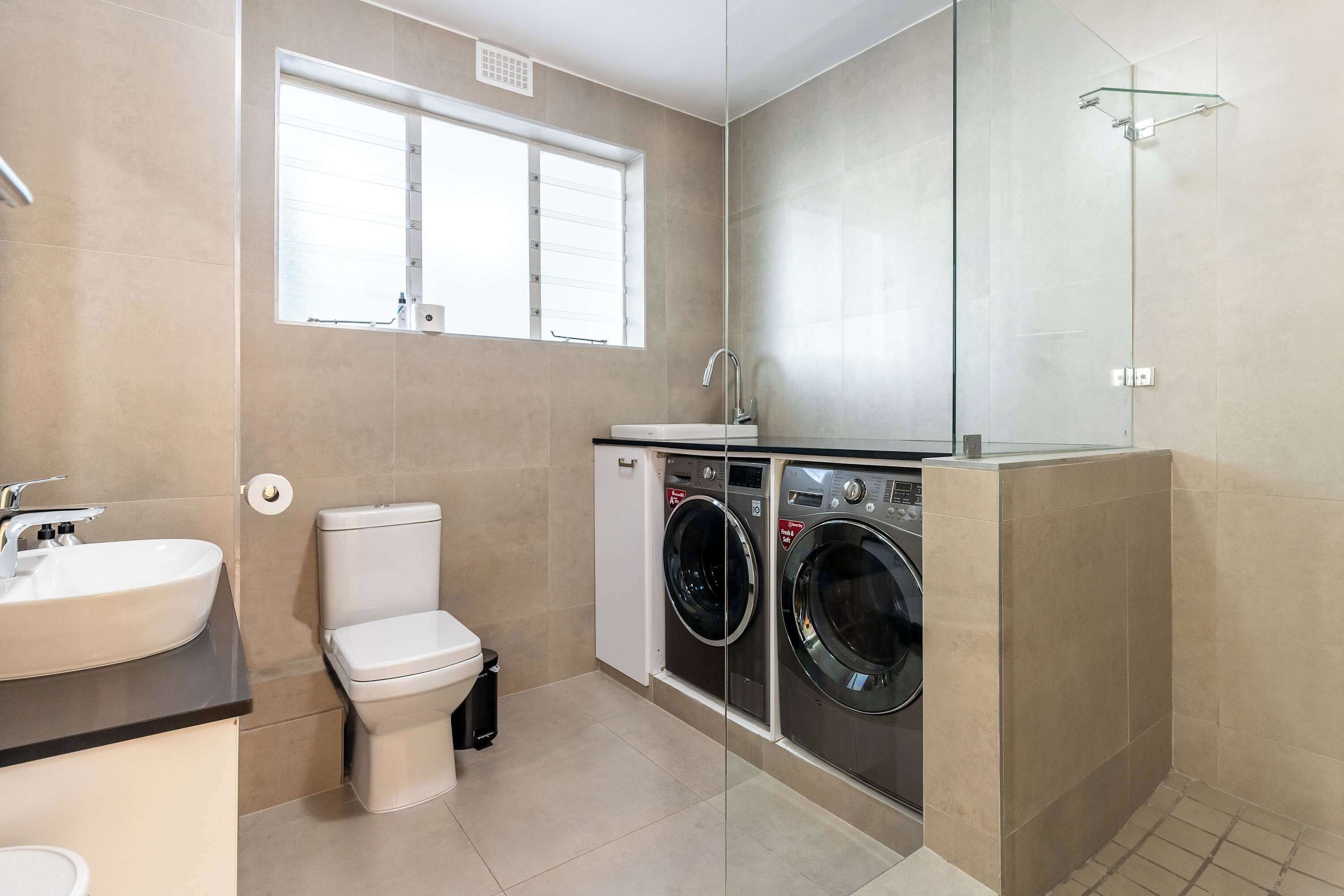 Baño con inodoro, lavamanos, lavadora y cabina de ducha de vidrio.