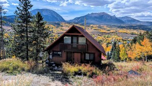 Eine Hütte mit Balkon, umgeben von Herbstlaub und Bergen im Hintergrund.