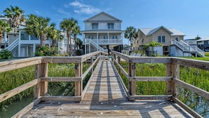 A wooden pier leading to a beachfront property with multiple houses, a clear blue sky, and palm trees. - Seven Bedroom Channel Front Home with a Private Pool and Hot Tub (Garden City Beach)