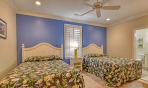 A bedroom with two beds, a window with blinds, a ceiling fan, and a nightstand with a lamp.