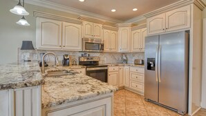 A kitchen with white cabinets, a stainless steel refrigerator, a microwave, and a granite countertop. - Seven Bedroom Channel Front Home with a Private Pool and Hot Tub (Garden City Beach)