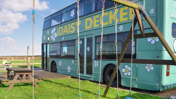 Un autobus à deux étages sur lequel on peut lire « DAISY DECKER », une balançoire et une table de pique-nique.
