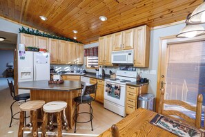 Une cuisine avec des meubles en bois, un four à micro-ondes, une cuisiniÚre et un coin repas équipé de tabourets.