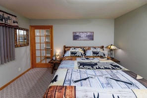 A bedroom with a bed, a nightstand, a lamp, a window with curtains, a door, and a wall-mounted picture.