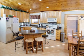 A kitchen with wooden cabinets, a central island, bar stools, a refrigerator, a microwave, and a stove. - Cabin in Lakewood right on Snowmobile Trails! (Lakewood)