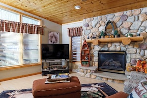 A living room with a stone fireplace, a television, and a wooden ceiling.