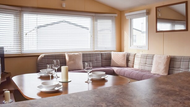 Una zona de estar acogedora con una mesa lista para comer, ventanas grandes con persianas y un espejo en la pared.