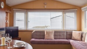 Un salón acogedor con un sofá, una televisión y una mesa de comedor con vasos y una vela.