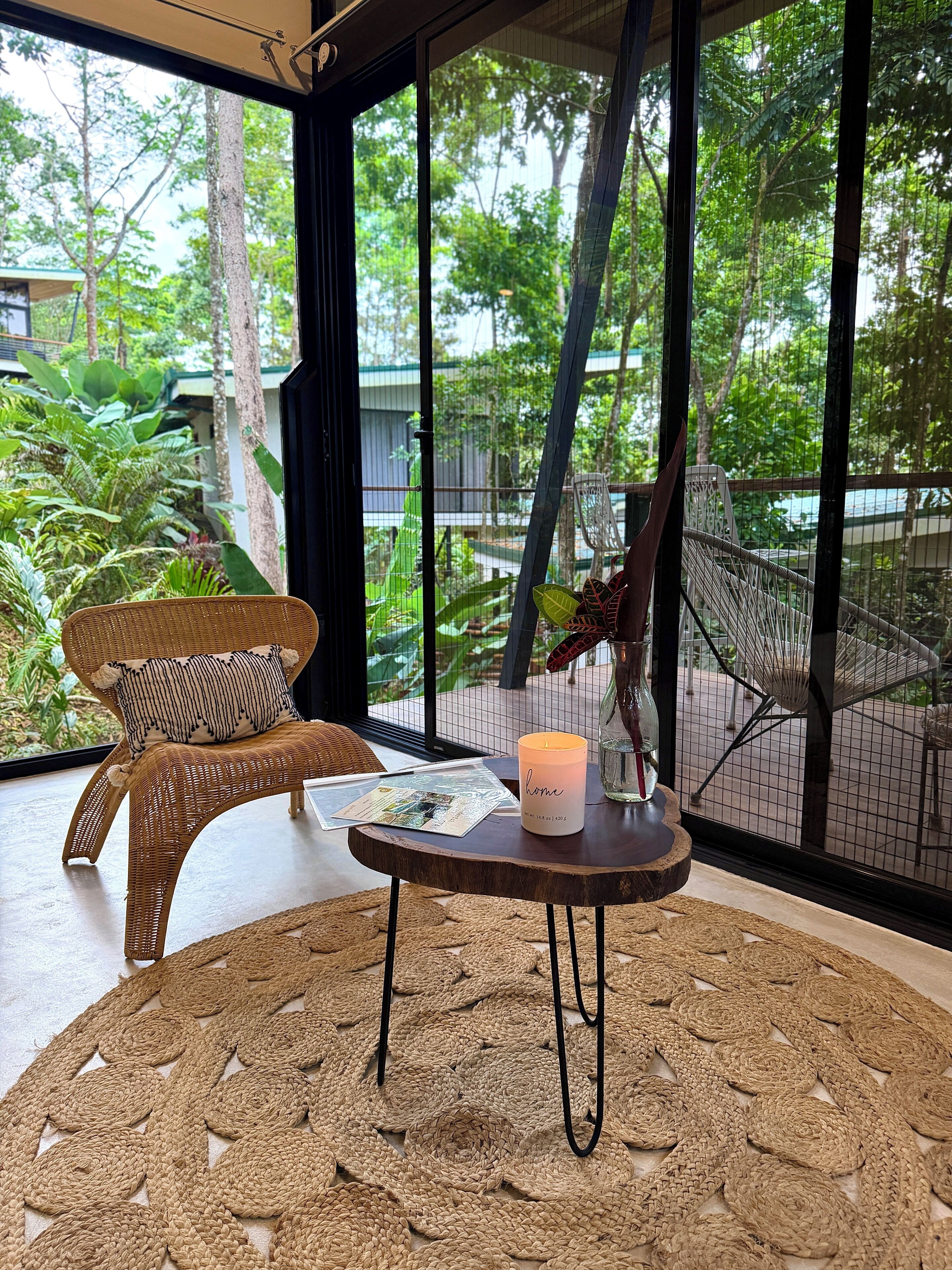 A wicker chair with a cushion, a small table with a candle, and a woven rug.