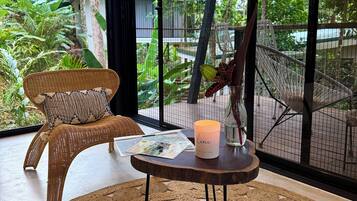 A wicker chair with a cushion, a small table with a candle, and a woven rug.