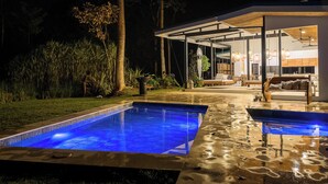 A modern outdoor pool area with a glass-enclosed lounge and a well-lit patio.