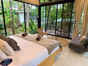 Une chambre dotée d’un grand lit, d’un fauteuil et offrant une vue sur un jardin luxuriant grâce à de grandes fenêtres.