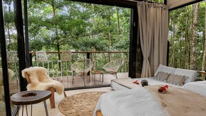 A bedroom with a large bed, two chairs, a small table, and a view of the forest. - The time is ripe for a pure relaxation experience (Quesada, San Carlos)