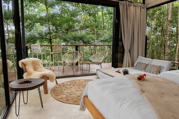 Une chambre avec un grand lit, deux fauteuils, une petite table et une vue sur la forêt.