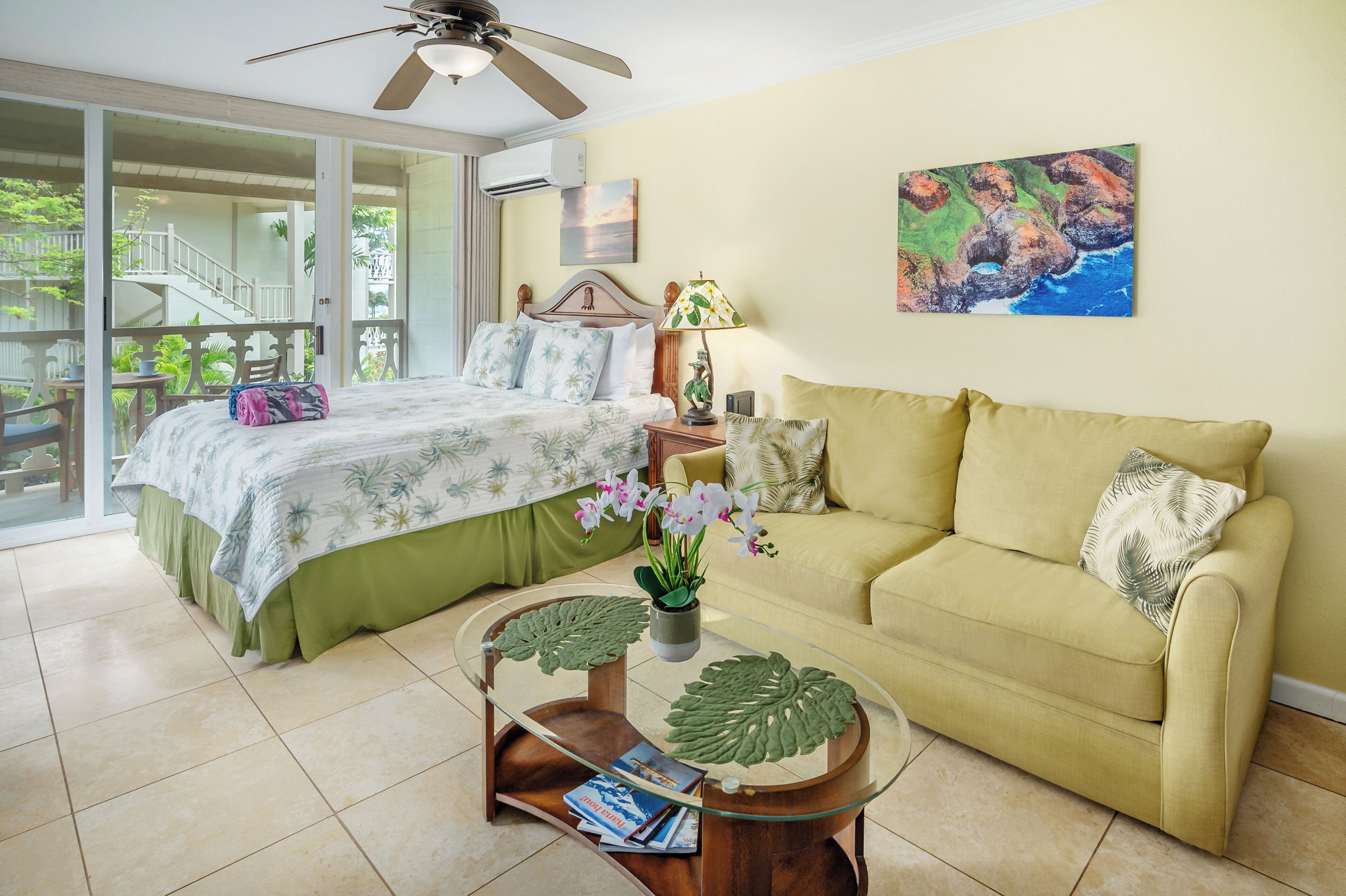 A bedroom with a bed, a sofa, a glass coffee table, and a painting on the wall.