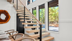 A modern staircase with wooden steps and black railings, leading to a room with large windows and a view of the outdoors. - Luxury Creekside Lodge for Group Gatherings (Broken Bow)