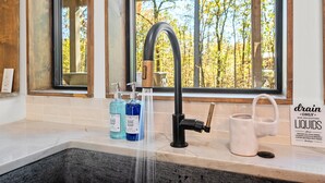 A kitchen with a modern faucet, a window with a view of trees, and dish soap bottles on the counter. - Luxury Creekside Lodge for Group Gatherings (Broken Bow)