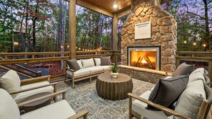 A cozy outdoor seating area with a stone fireplace, wooden furniture, and a view of the forest. - Luxury Creekside Lodge for Group Gatherings (Broken Bow)