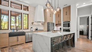 A modern kitchen with a large island, stainless steel appliances, and a view of the outdoors. - Luxury Creekside Lodge for Group Gatherings (Broken Bow)