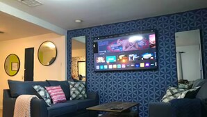 A living room with a large flat-screen TV mounted on the wall, a blue patterned wall, a dark blue sofa, and a wooden coffee table. - 2 Bdrm 2bath Downtown Permit # 4768 (Palm Springs)