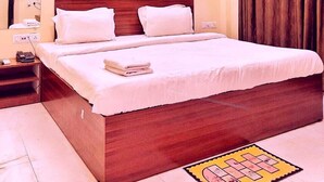 A hotel room with a wooden bed, white linens, a bedside table with a phone, and a wall-mounted air conditioner. - The Moonlight Resort Indore (Sanwer)
