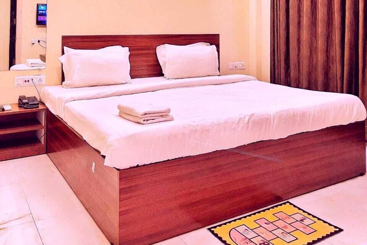 Habitación de hotel con cama de madera, ropa de cama blanca, mesita de noche con teléfono y aire acondicionado instalado en la pared.