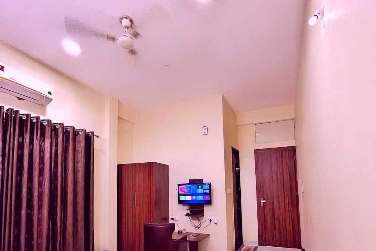 Una habitación pequeña y bien iluminada con una cama, un escritorio, un televisor y un ventilador de techo.