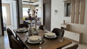 Un comedor con una mesa de madera dispuesta para cuatro personas, rodeada de sillas. Hay un jarrón con flores sobre la mesa, y una mesita auxiliar con un objeto decorativo.
