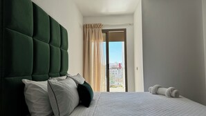 Habitación de hotel con una cama grande, cabecera verde y vista a la ciudad desde la ventana.