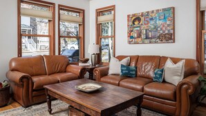 Ein Wohnzimmer mit zwei braunen Ledersofas, einem Holztisch und einem farbenfrohen abstrakten Gemälde an der Wand.