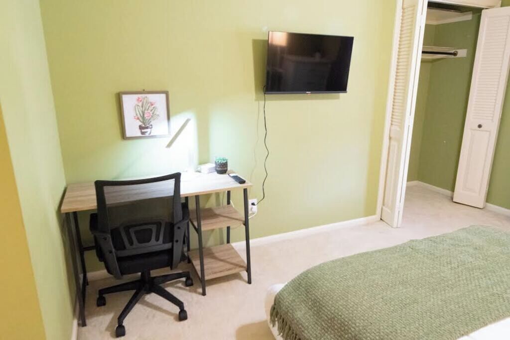 Een slaapkamer met een bed, een bureau met stoel, een televisie en een deur.