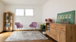Una habitación con dos sillas moradas, un armario de madera, un cuadro y una ventana.