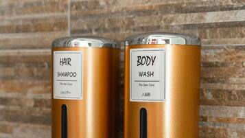 Zwei an der Wand montierte, metallische, zylinderförmige Spender mit den Aufschriften 'HAIR SHAMPOO' und 'BODY WASH' an einer strukturierten Wand.