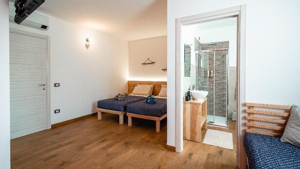 Una habitación con dos camas, un baño pequeño con ducha de vidrio y un banco de madera.