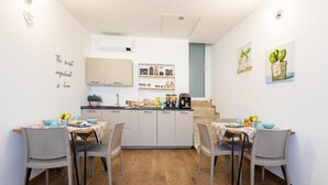 Cocina compacta con isla central, muebles blancos y una pequeña zona de comedor con dos sillas.