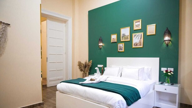 A hotel room with a large bed, a nightstand, a vase with flowers, and framed pictures on the wall. - Charming Oasis in the Heart of Cairo – Authentic Hospitality Awaits! (Cairo Governorate)