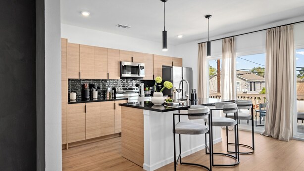 A modern kitchen with wooden cabinets, a black countertop, and a central island with bar stools.