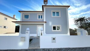 A two-story house with a grey facade and a tiled roof. There is a white entrance with a door and a small window above it.