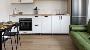A modern kitchen with white cabinets, a black oven, a stainless steel refrigerator, and a green sofa.