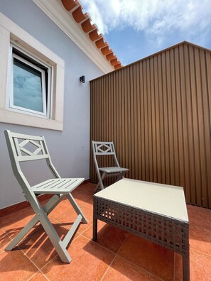 Un patio al aire libre con dos sillas, una mesa, una ventana y una valla de madera.