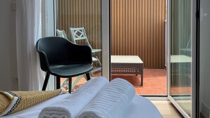 A hotel room with a bed, a chair, a small table, and a view of a wooden fence through a sliding glass door.
