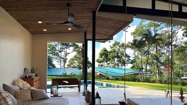 A modern living room with a sofa, a coffee table, and a swing chair, overlooking a pool and lush greenery. - The time has come to immerse yourself in incomparable relaxation (Quesada, San Carlos)