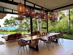 Un área de comedor al aire libre con sillas de mimbre, una mesa de madera y lámparas colgantes de mimbre.