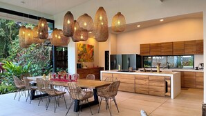 A modern kitchen with wooden cabinets, a central island, and a dining area with wicker chairs and a wooden table. - The time has come to immerse yourself in incomparable relaxation (Quesada, San Carlos)