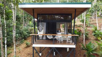 A wooden deck with chairs and a hammock, surrounded by trees.