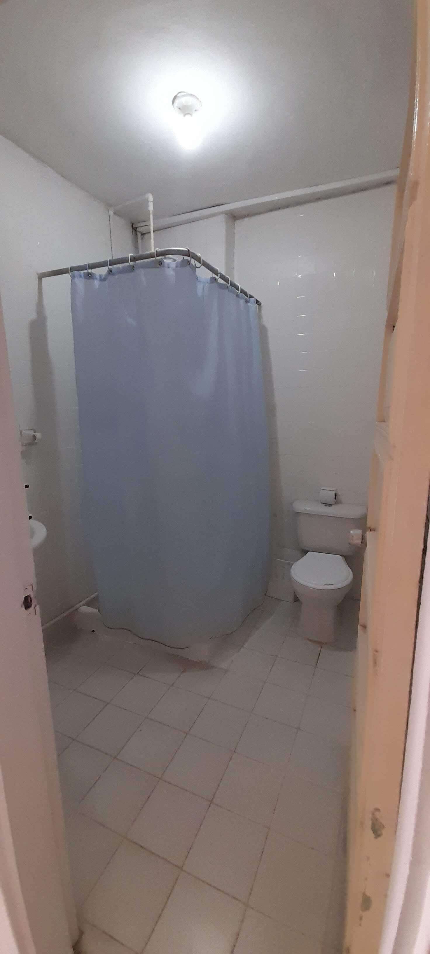 A small, tiled bathroom with a shower curtain, a toilet, and a visible pipe on the ceiling.