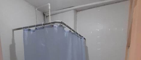 A small, tiled bathroom with a shower curtain, a toilet, and a visible pipe on the ceiling.