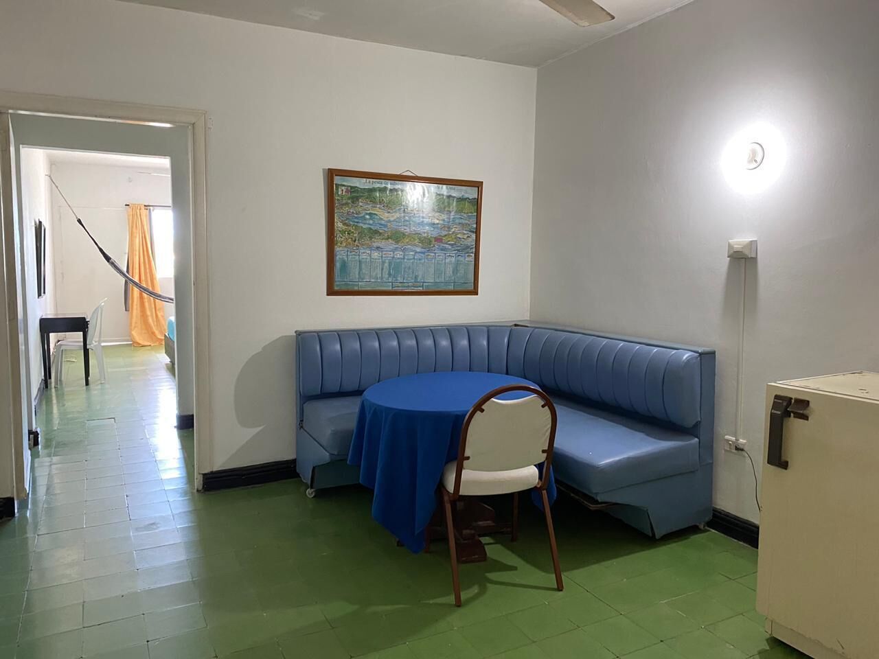 Egy szoba, melyben egy kék kanapé, egy kerek, kék terítővel borított asztal és egy falfestmény található.