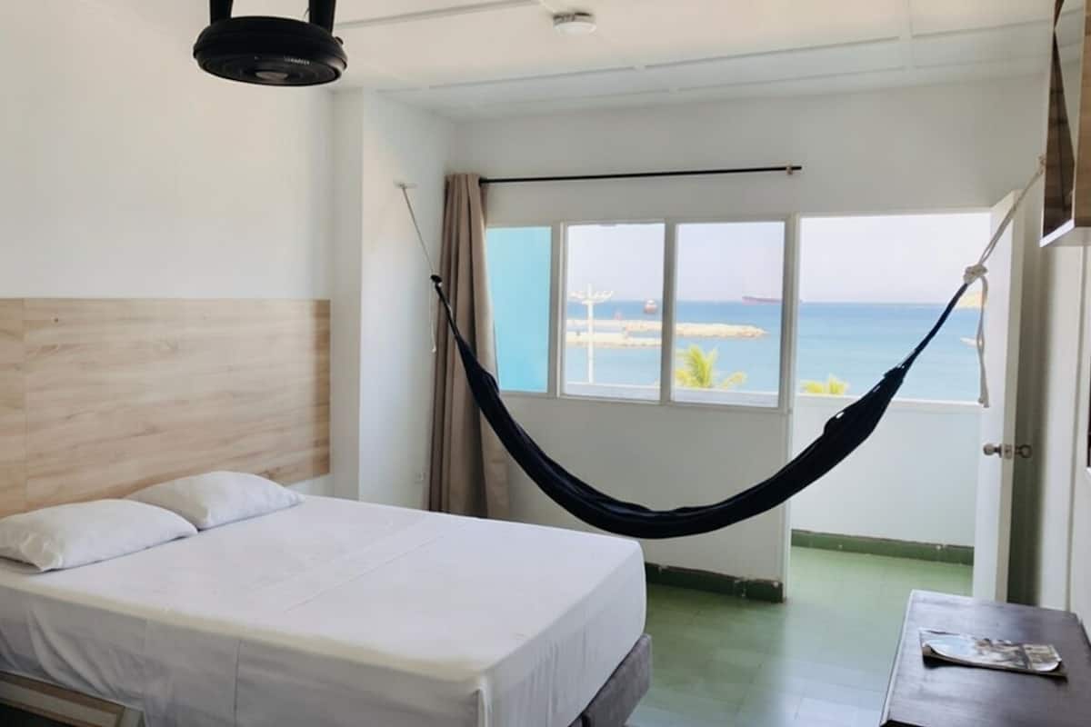 A hotel room with a bed, a hammock, a view of the sea, and a balcony.
